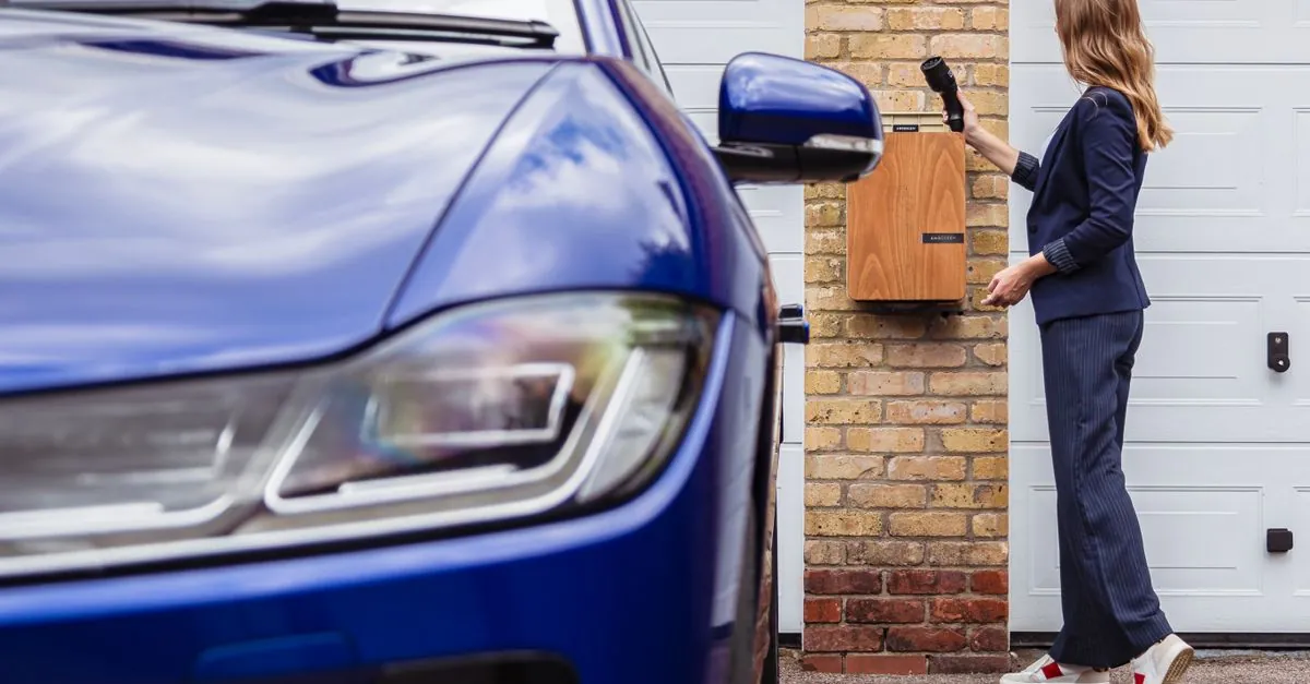 Vrouw gebruikt een laadpaal aan de gevel naast haar elektrische wagen